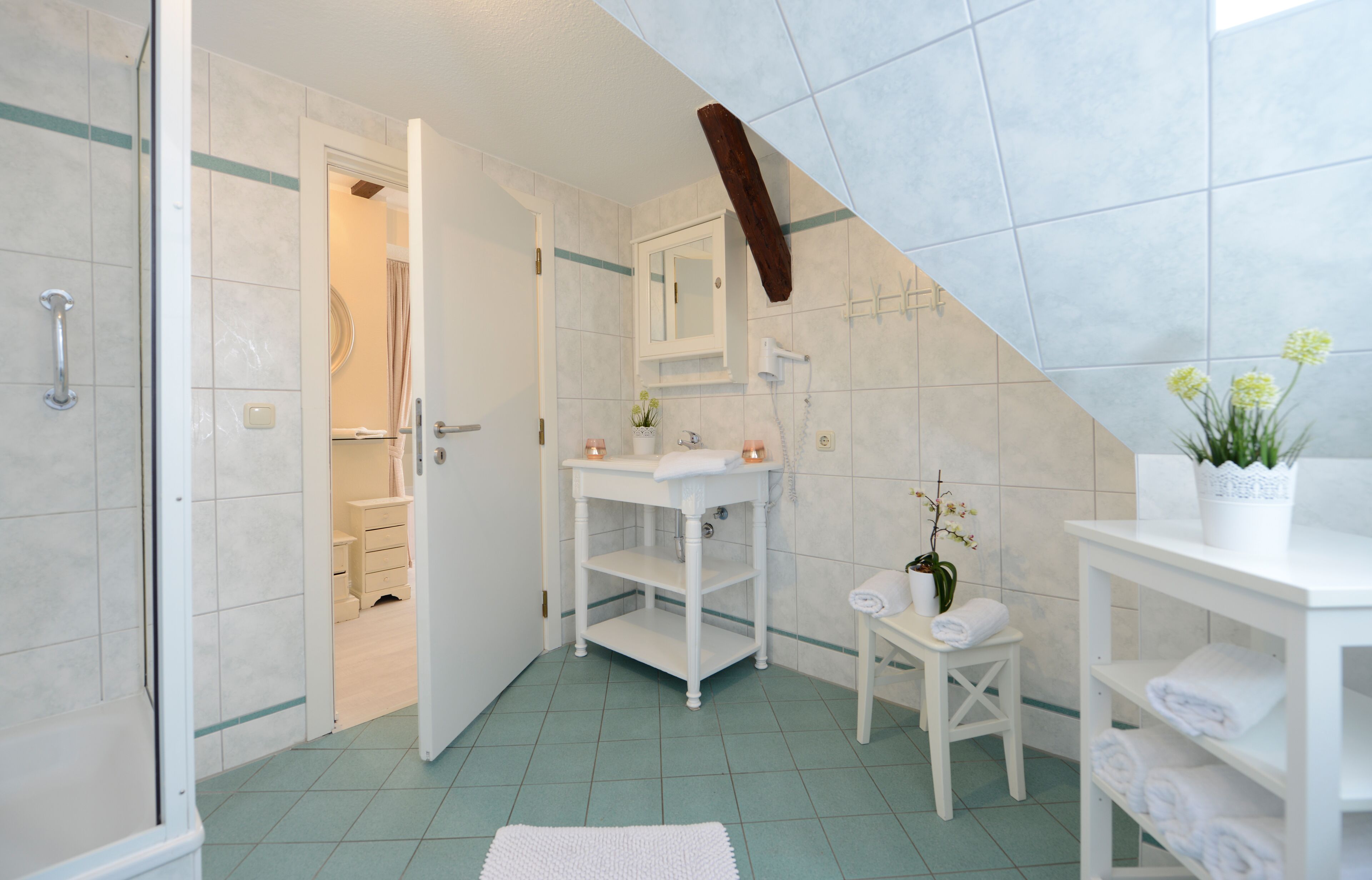 Ein Badezimmer mit Dusche, Waschbecken, Spiegel, Handtuchhalter und einer kleinen Pflanze.