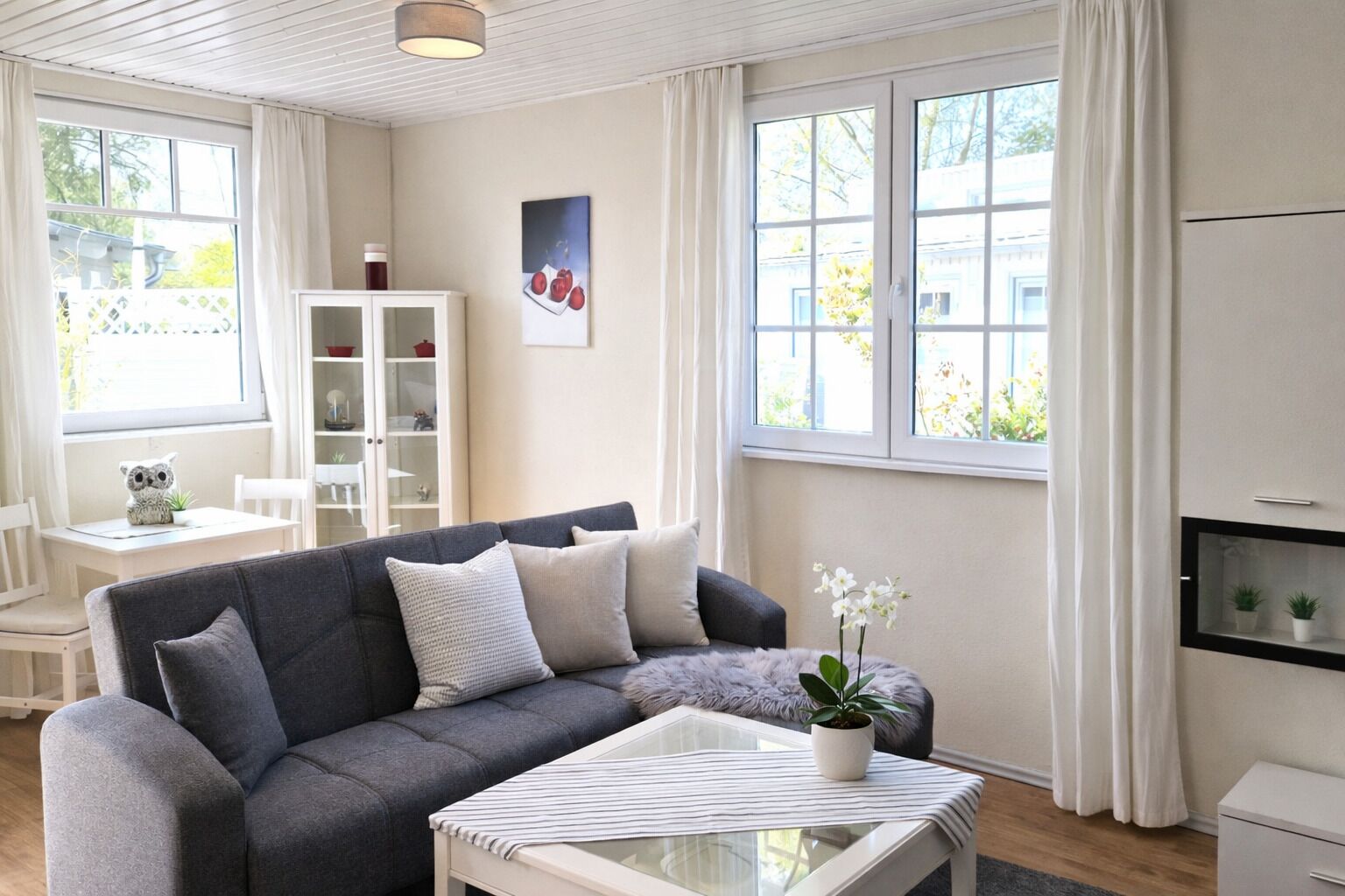 En stue med en grå sofa, et glasbord, et hvidt skab og et vindue med gardiner.