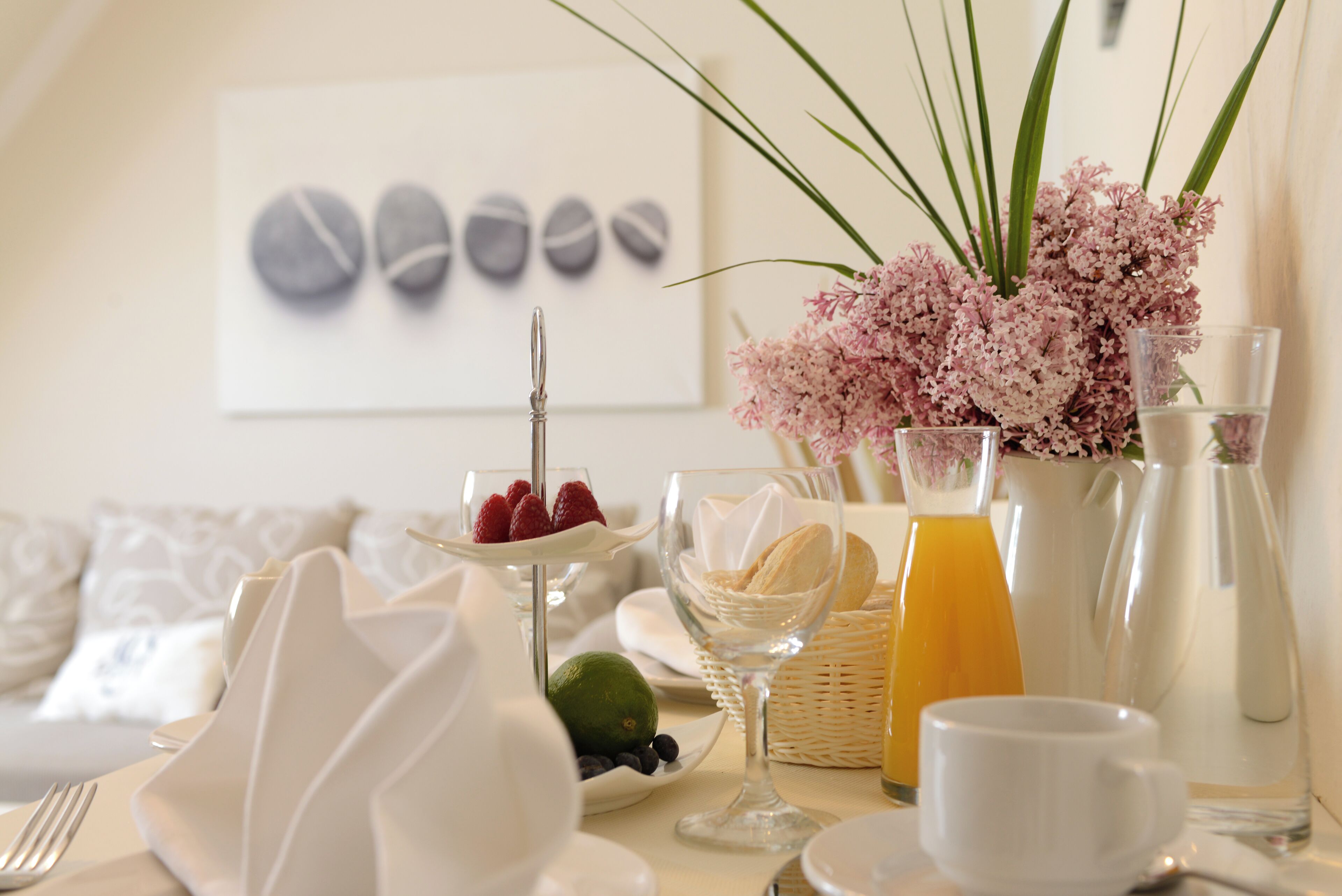 A breakfast setting with a table set for two, featuring a plate of strawberries, a glass of orange juice, and a vase of flowers.