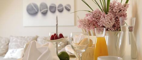 A breakfast setting with a table set for two, featuring a plate of strawberries, a glass of orange juice, and a vase of flowers.