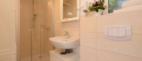 Un baño moderno con ducha de vidrio, un lavamanos blanco y un espejo sobre él.
