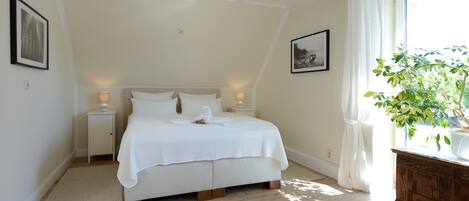 A neatly arranged bedroom with a bed, bedside tables, a nightstand, a potted plant, and a window with curtains.