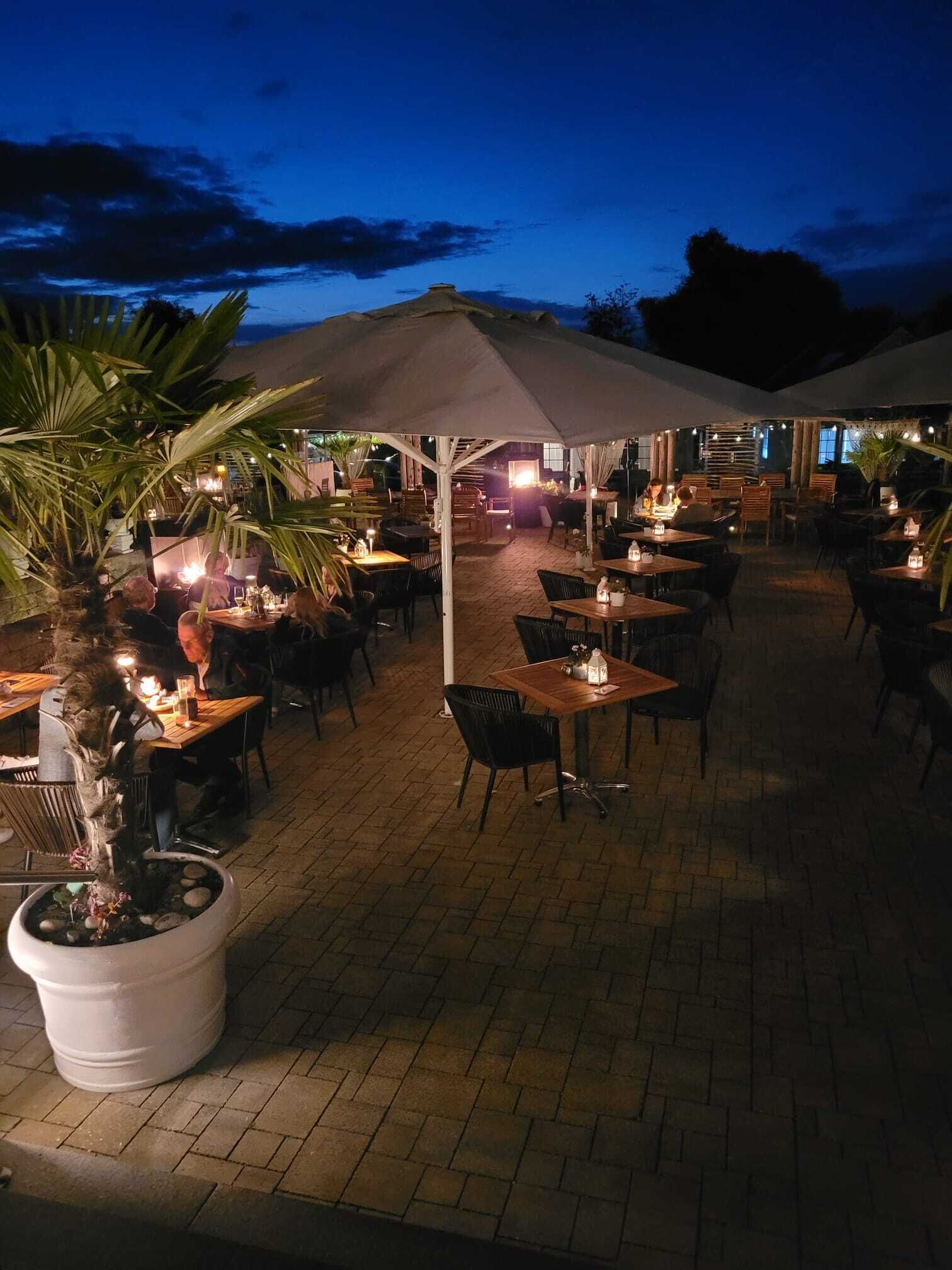 An outdoor dining area with tables and chairs, umbrellas, and potted plants.
