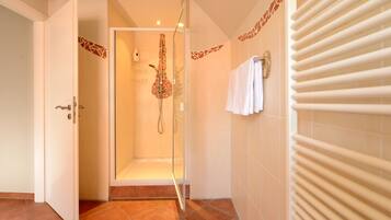 Un baño moderno con ducha envuelta en vidrio, un toallero blanco y suelo de baldosas.