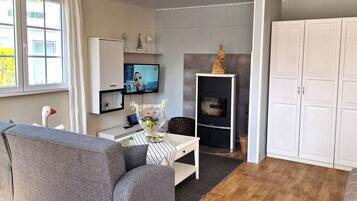 A modern living room with a grey sofa, a flat-screen TV, a fireplace, and white cabinets.