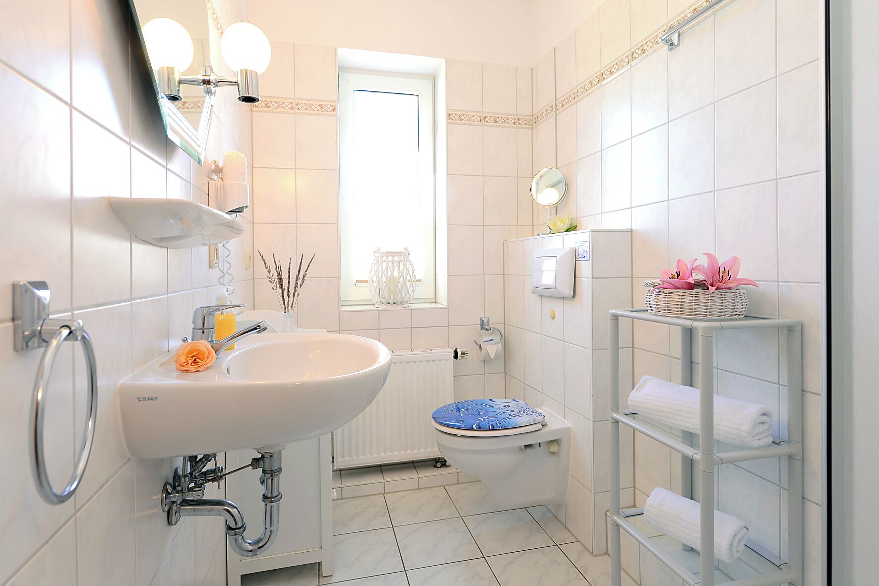 A modern bathroom with a white sink, a toilet with a blue seat, a towel rack, and a mirror.