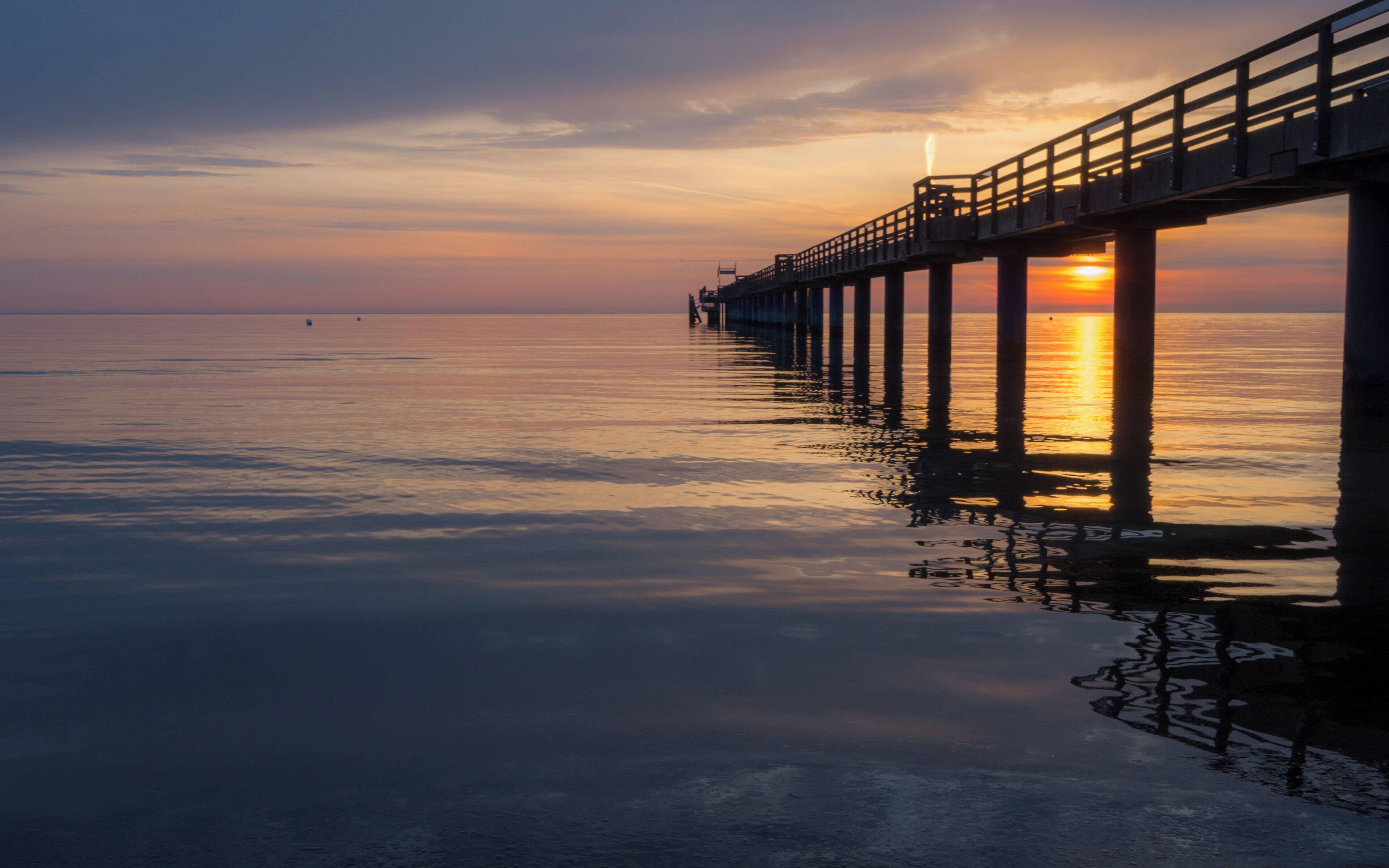 Un muelle se adentra en aguas tranquilas al atardecer.