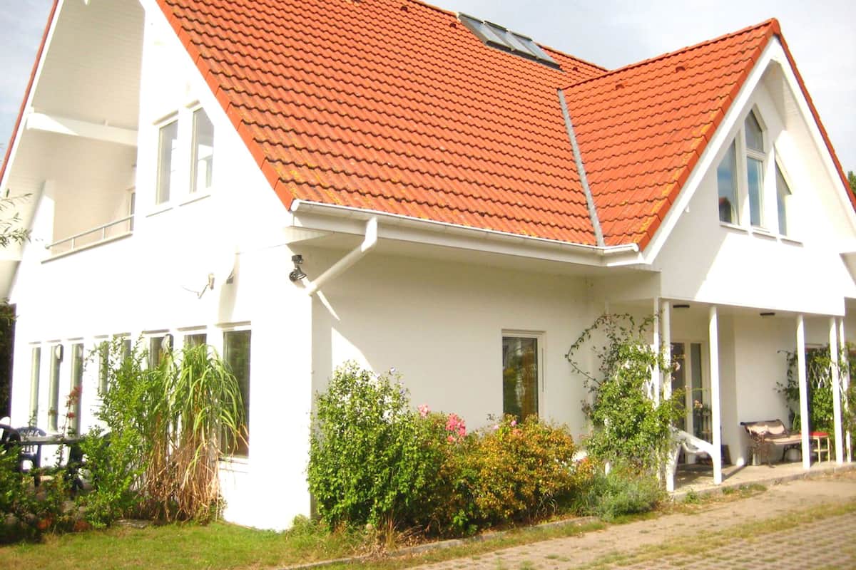 Ett tvåvåningshus med ett rött tegeltak, vita ytterväggar och en veranda med en bänk.
