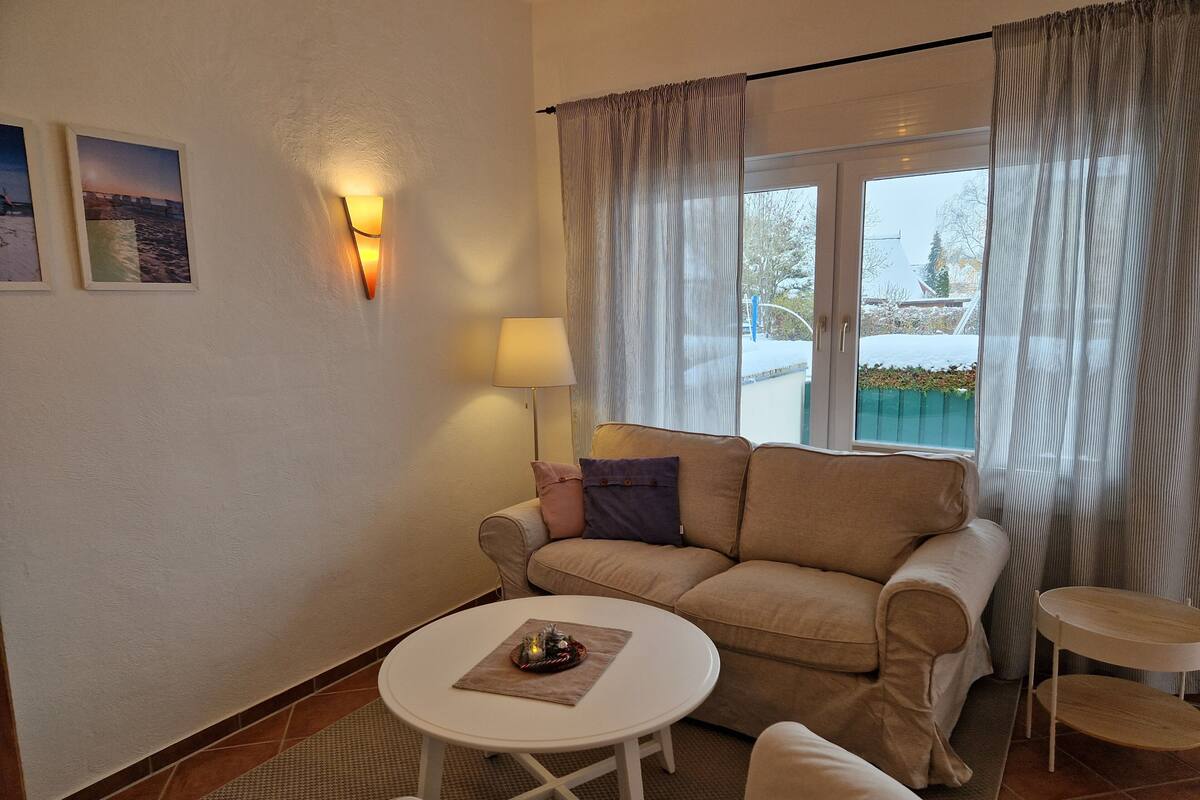 Ett vardagsrum med en soffa, ett litet runt bord, en lampa och utsikt över en pool genom ett fönster.