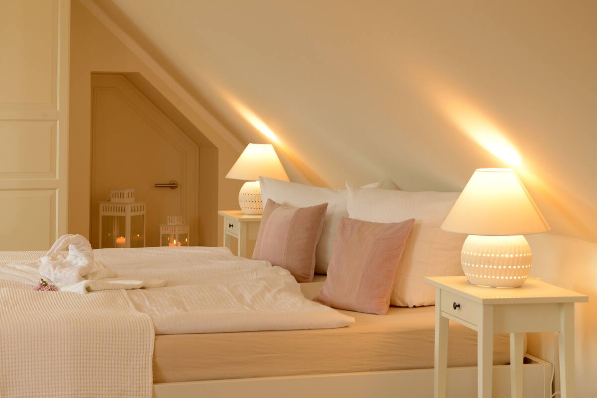 Ett hotellrum med en väl bäddad säng, två sänglampor och en dörr som leder till ett annat rum.