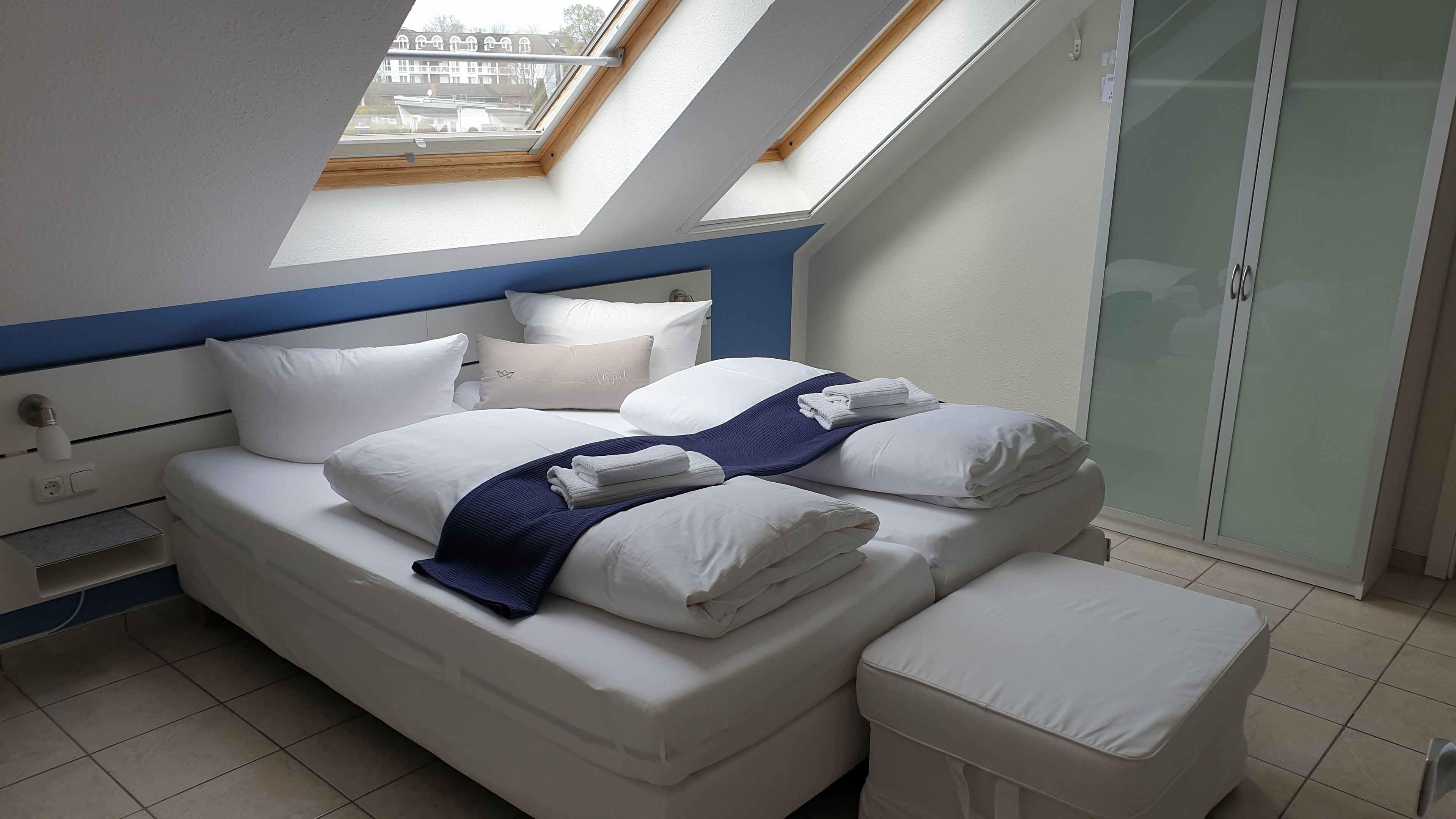 A modern bedroom with a skylight, a large bed with white linens, and a glass door leading to a balcony.