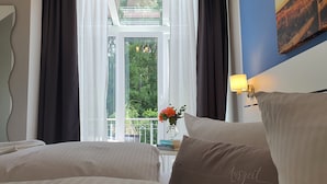 A hotel room with two beds, a window with curtains, a vase with flowers, and a painting on the wall. - Hotel Garni Auszeit (Boltenhagen)