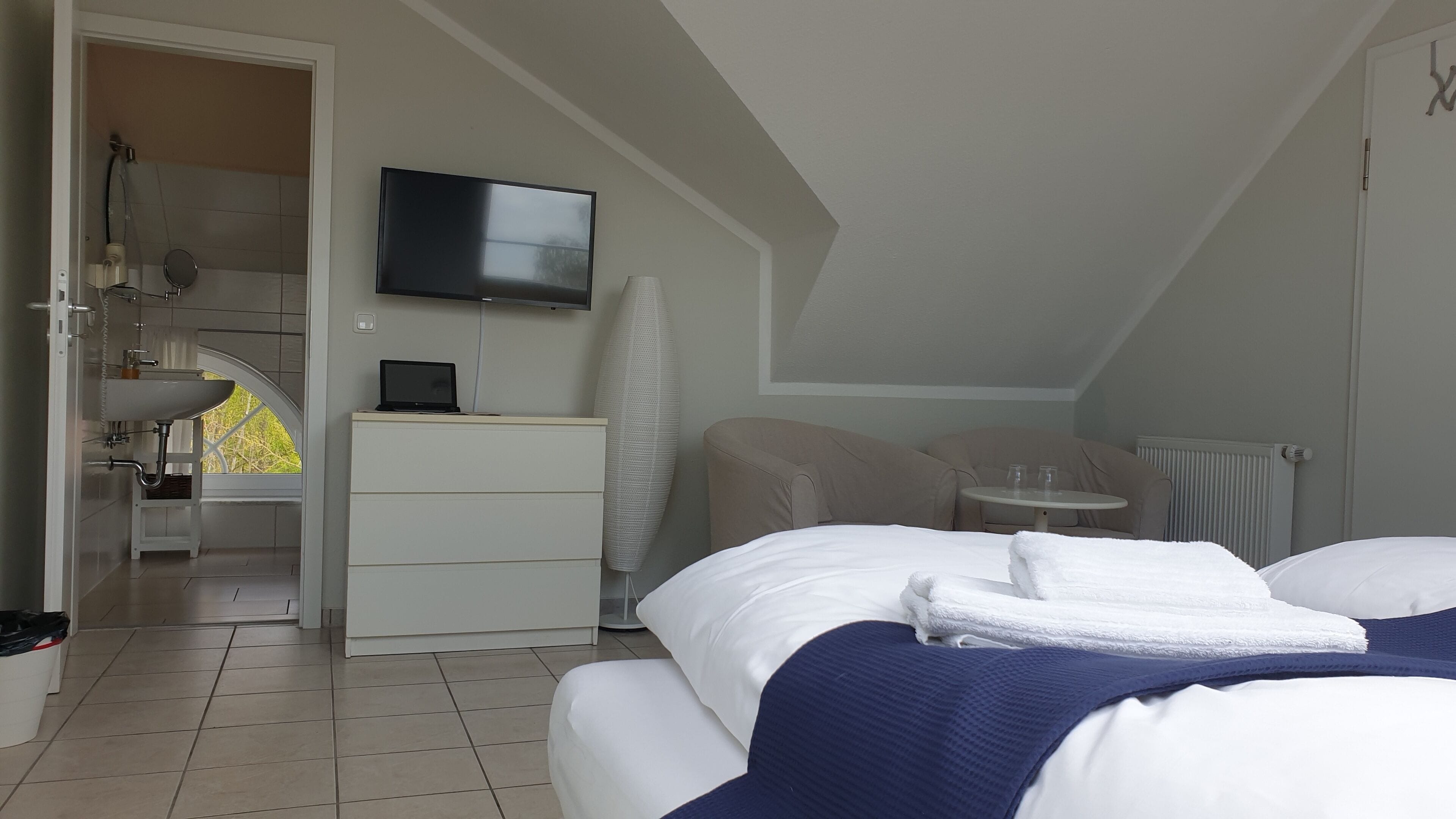 Una habitación de hotel moderna con cama, escritorio, televisor y baño con lavamanos y ducha.