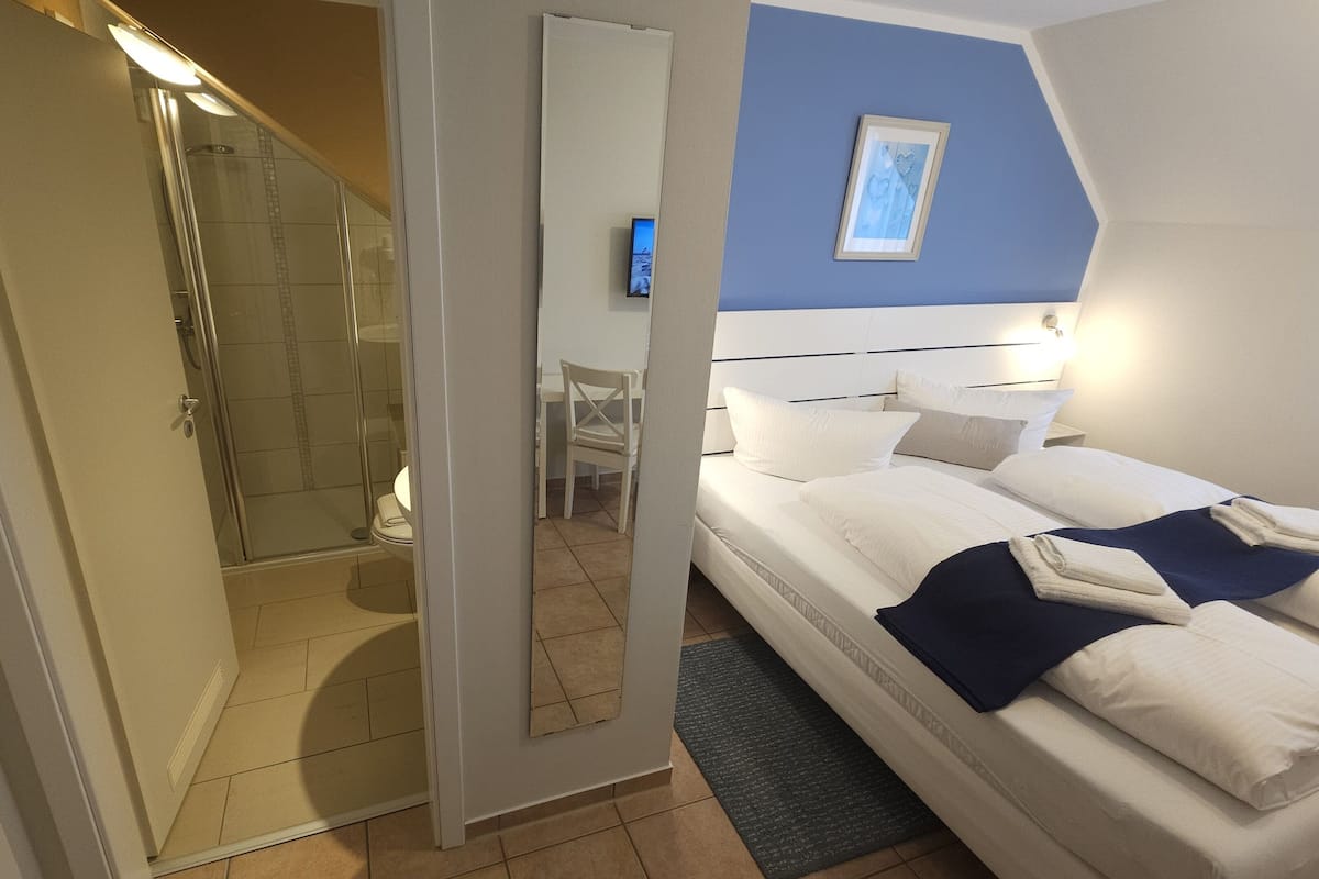 A hotel room with a bed, a desk, a chair, and a shower area.