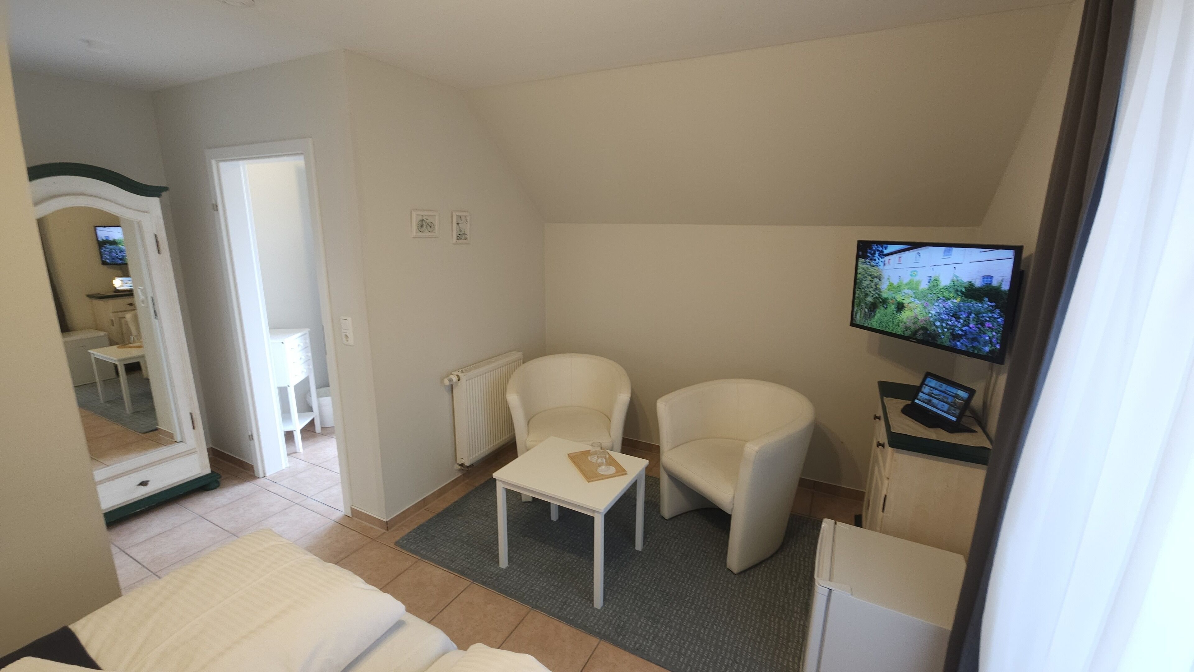 Et hotelværelse med en seng, to stole, et lille bord, et fjernsyn og et badeværelse, der ses gennem en åben dør.