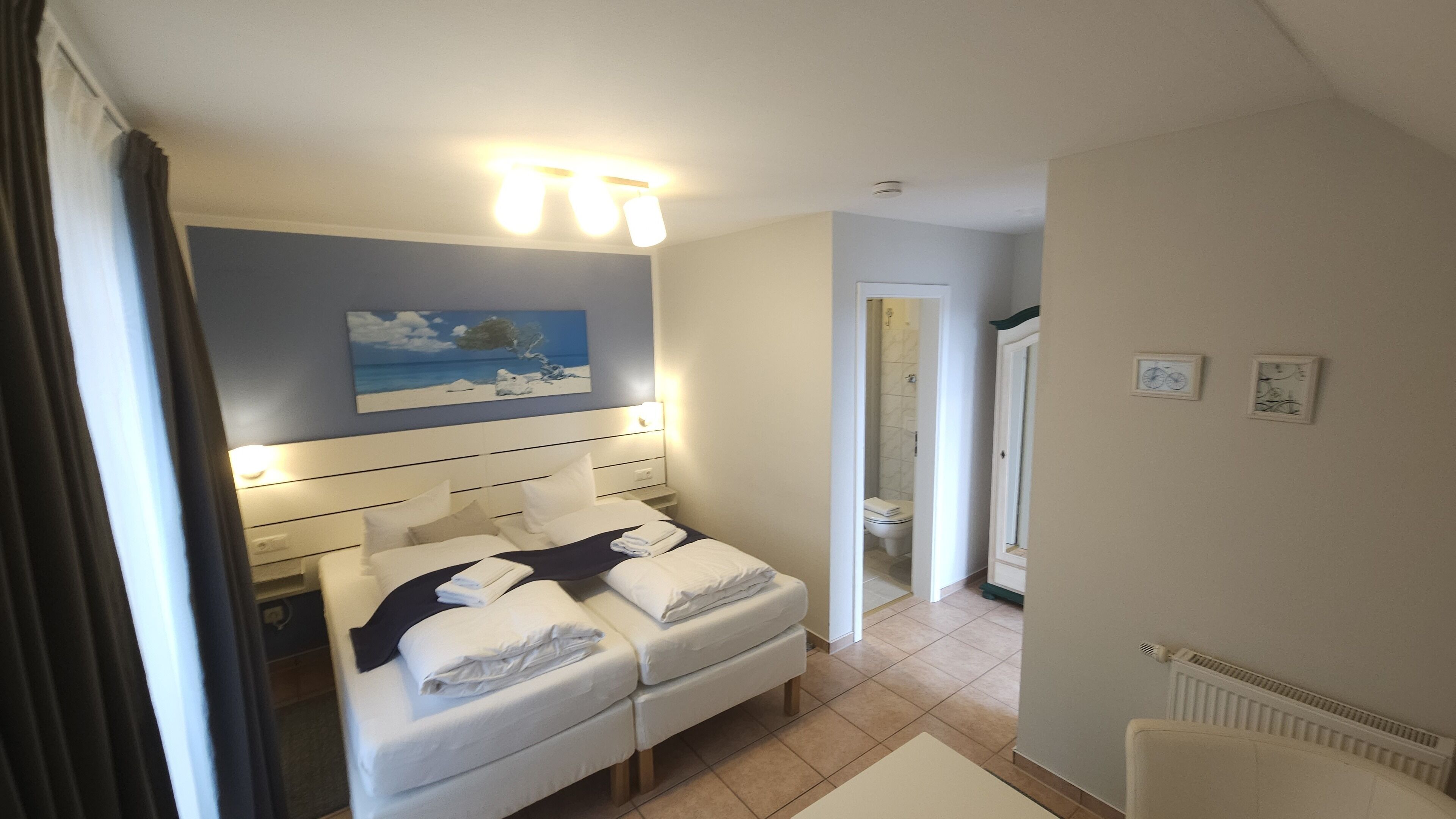 Ein Hotelzimmer mit Bett, Nachttischen, einem Gemälde und einem durch eine offene Tür sichtbaren Badezimmer.