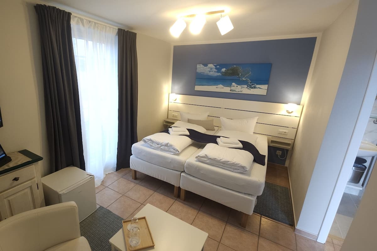 A hotel room with a bed, a desk with a computer, a TV, and a painting on the wall.