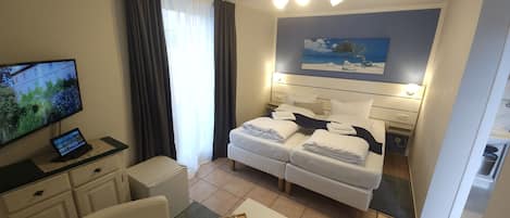 Habitación de hotel con cama, escritorio, computadora, televisor y un cuadro en la pared.