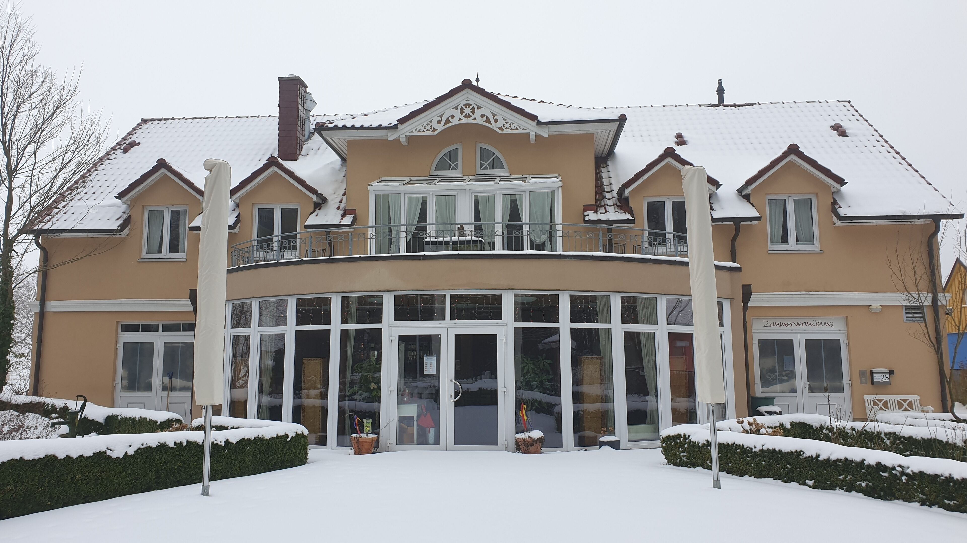 A two-story building with a curved glass facade, multiple balconies, and a snow-covered roof.