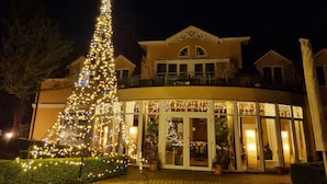 A large, illuminated Christmas tree in front of a hotel with a grand entrance and multiple windows. - Hotel Garni Auszeit (Boltenhagen)