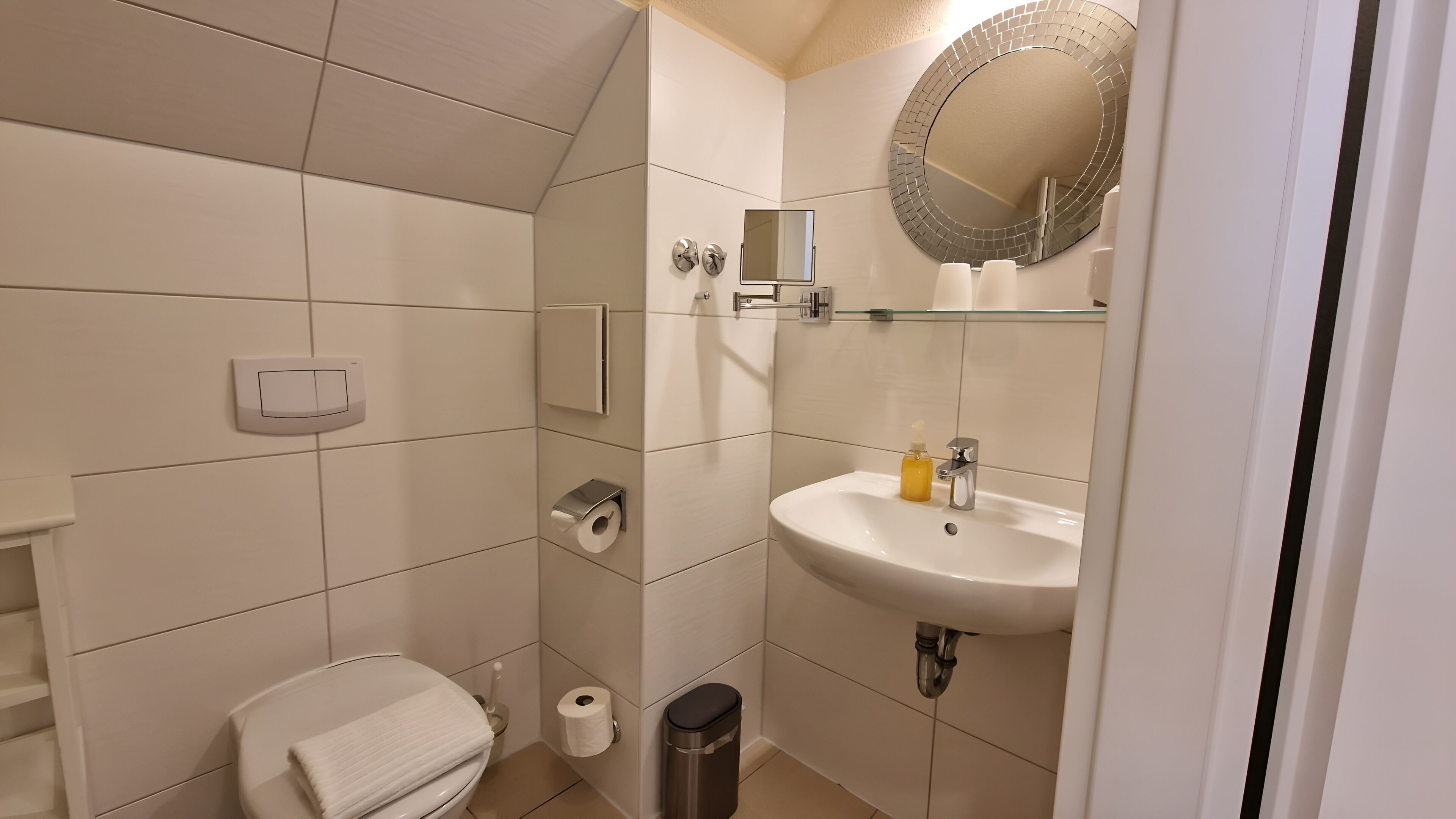 A modern bathroom with a toilet, a sink, a mirror, and a trash bin.