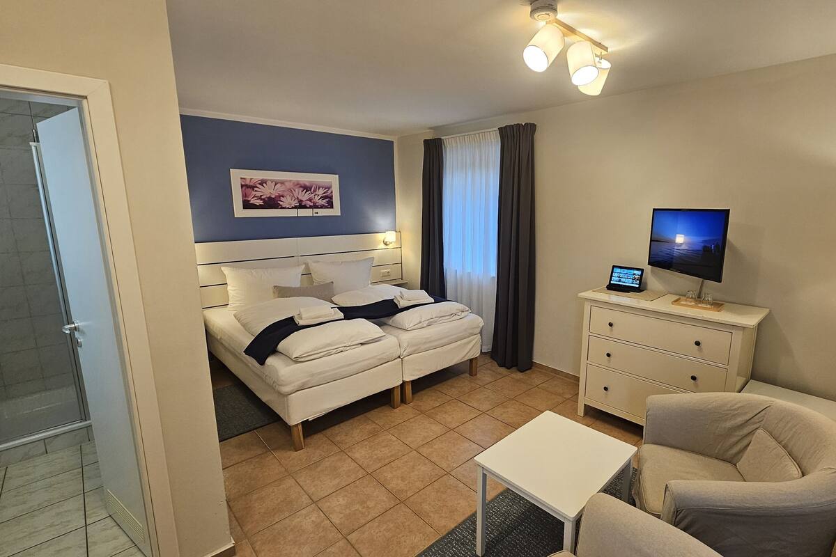 A hotel room with a bed, a desk, a chair, a TV, and a bedside table.