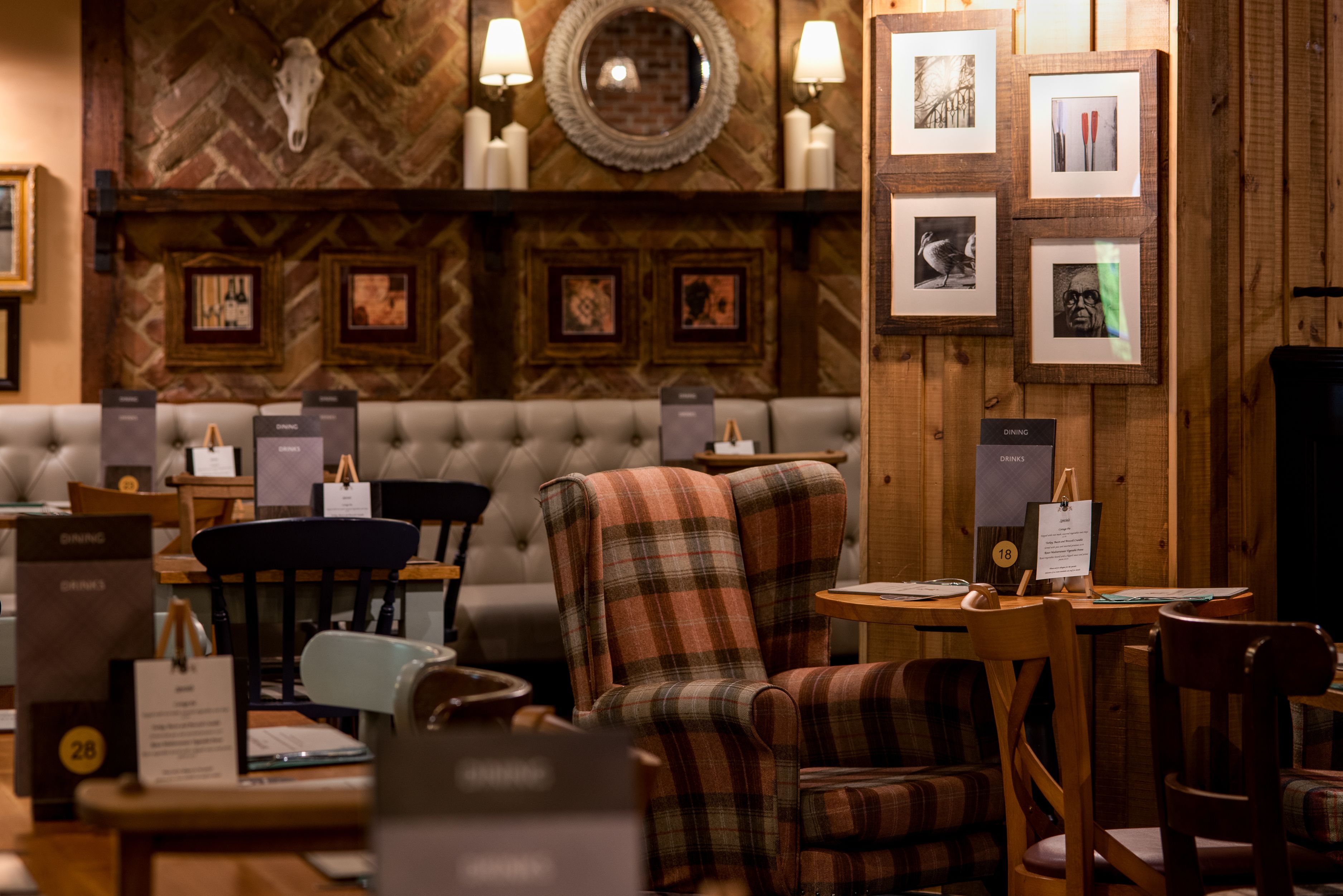 Un acogedor interior de restaurante con pared de madera, sofá capitonado, sillas a cuadros y cuadros enmarcados en la pared.