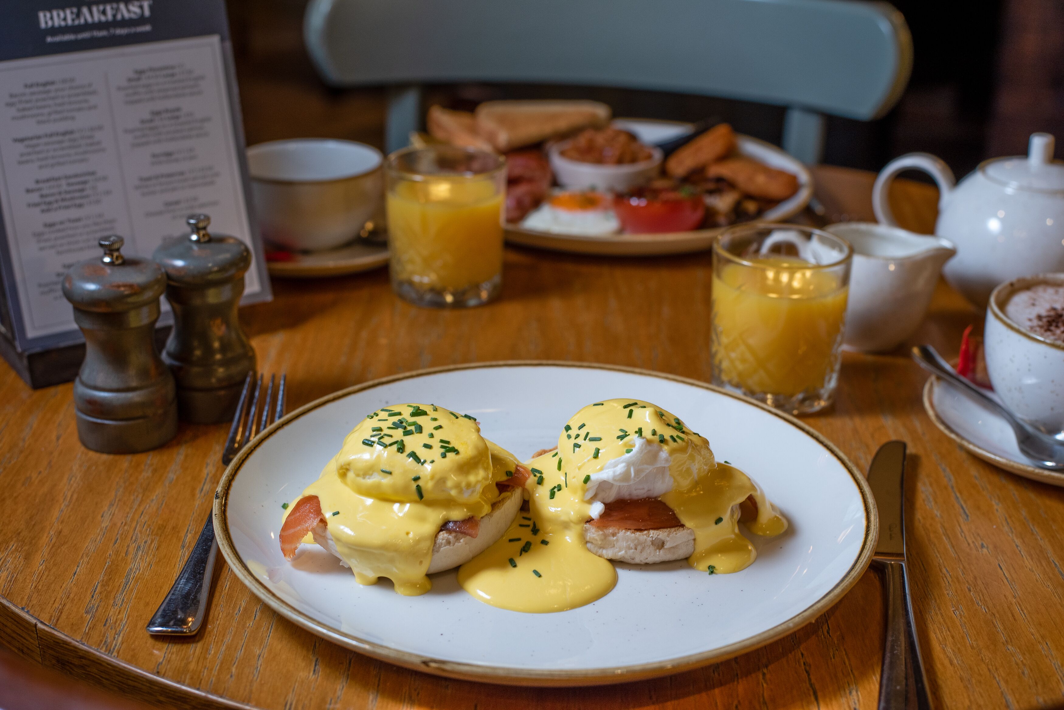 Een ontbijtsetting met Eggs Benedict, toast en sinaasappelsap op een houten tafel.