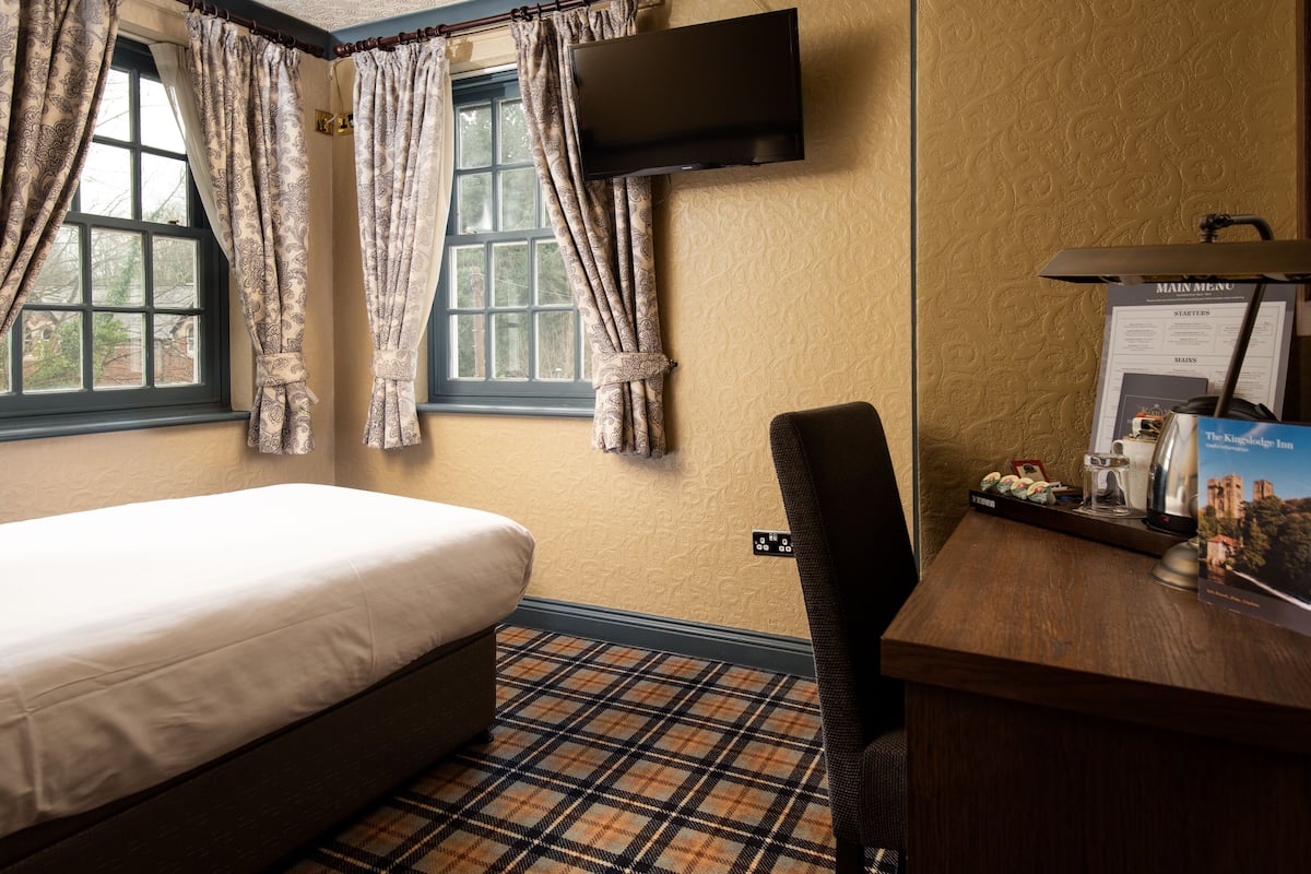A hotel room with a bed, a desk with a computer, a flat-screen TV, and a window with curtains.