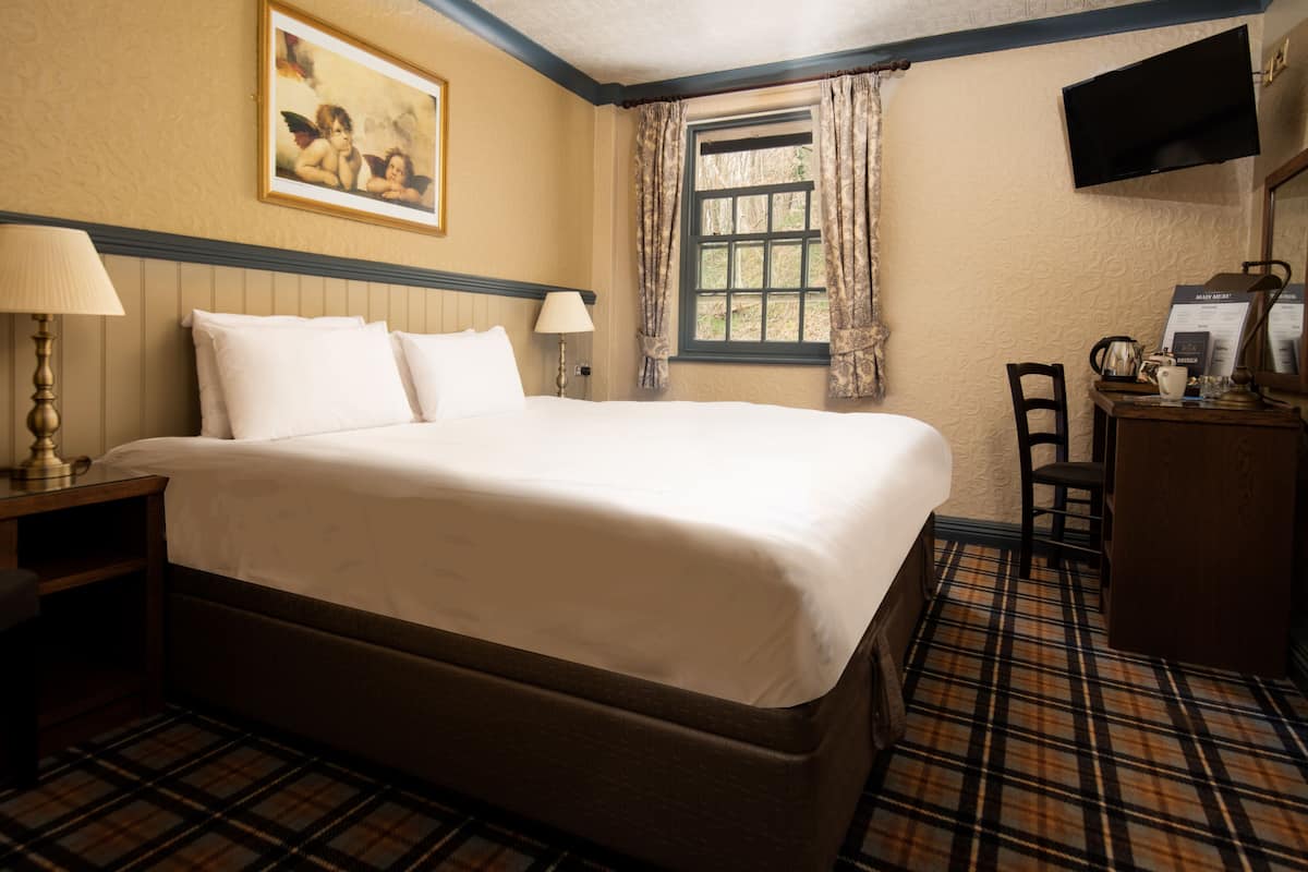 A hotel room with a large bed, a desk with a chair, a television, and a window with curtains.