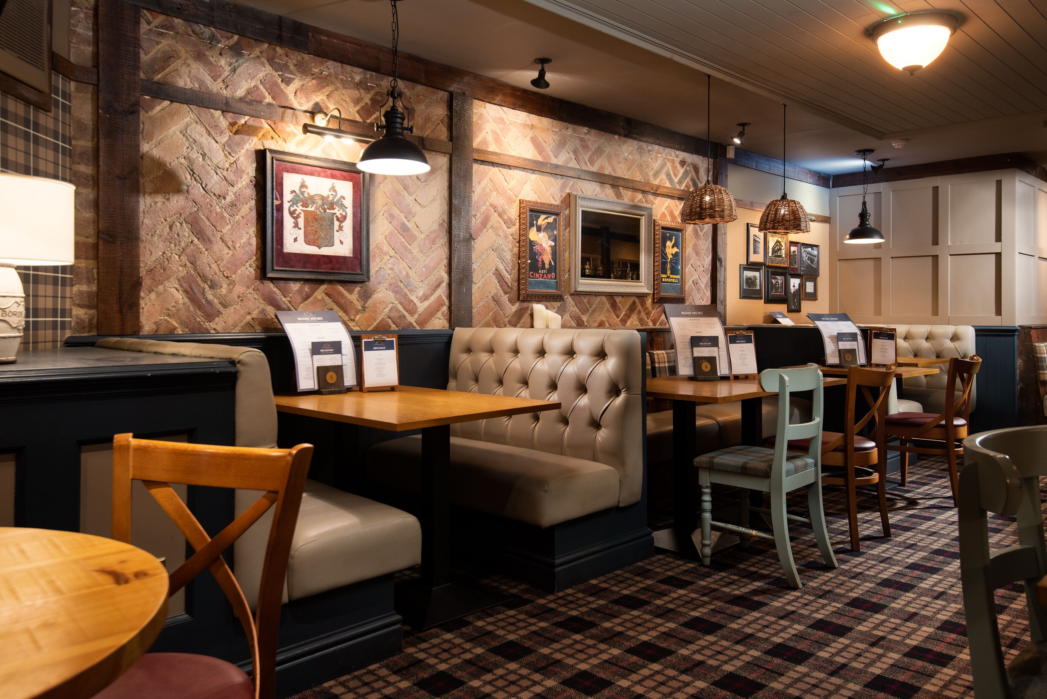 A restaurant interior with wooden tables, cushioned booths, and hanging pendant lights.