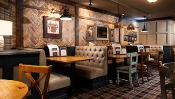 A restaurant interior with wooden tables, cushioned booths, and hanging pendant lights.