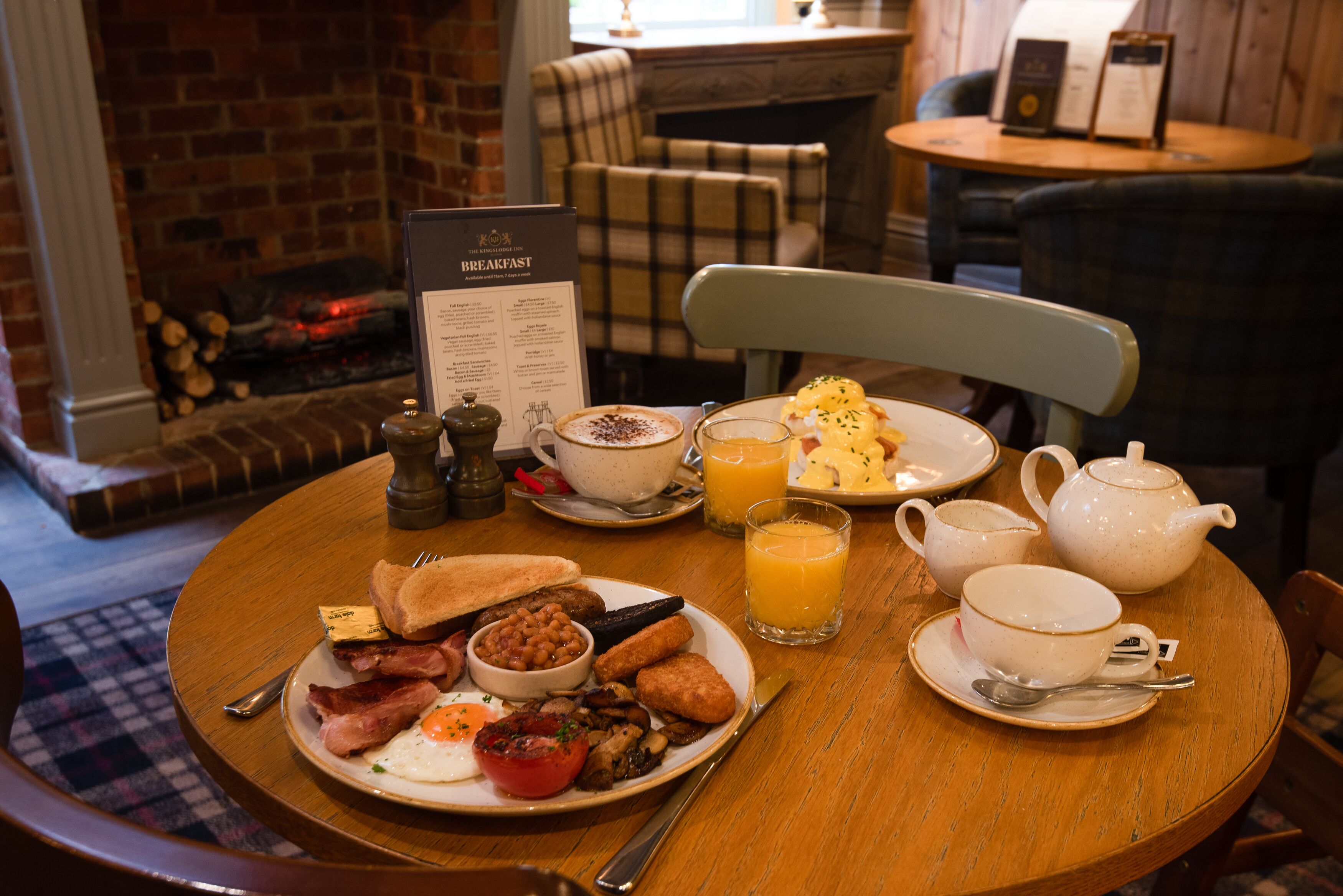A breakfast table with a menu, a teapot, cups, and a glass of orange juice.