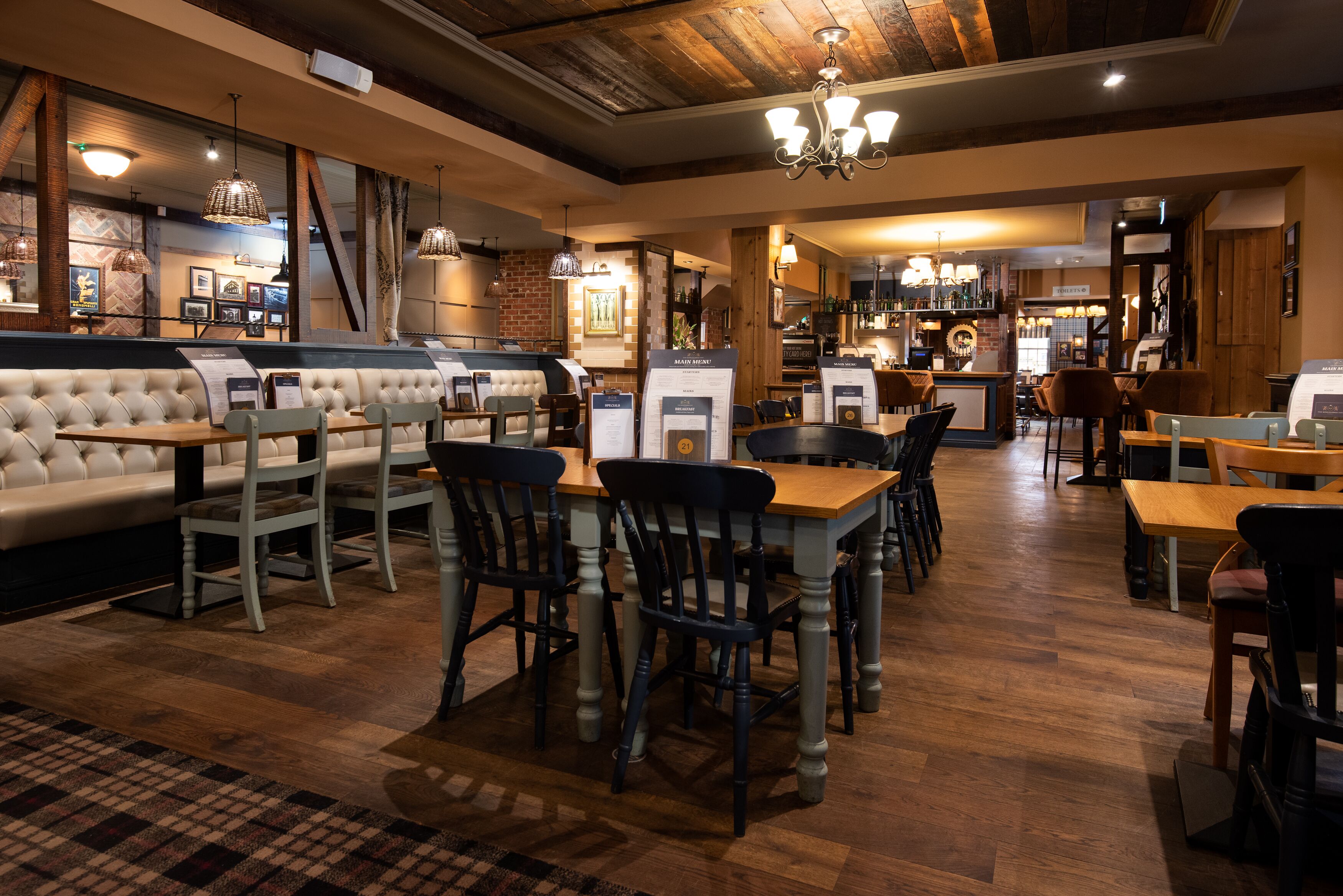 A restaurant with a bar area, wooden flooring, and a mix of seating options including tables and a sofa.