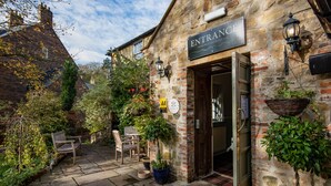 A stone building with a sign reading "ENTRANCE" and a welcoming sign above the door. There are outdoor seating areas with chairs and tables, and potted plants around. - The Kingslodge Inn - The Inn Collection Group (Durham)