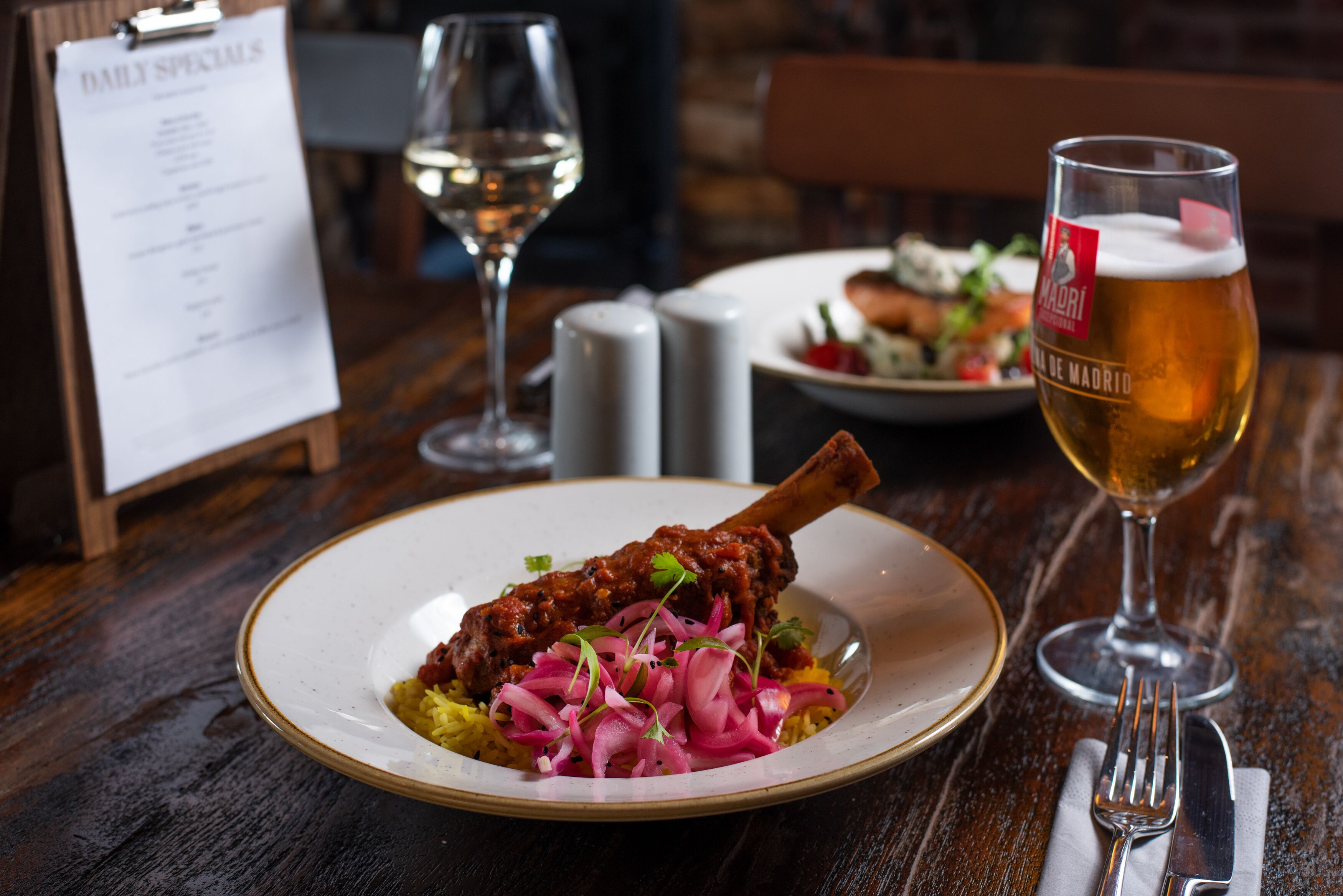 Une table à manger avec une assiette de nourriture, un verre de bière et un menu.