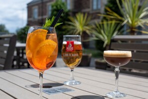 Three glasses of beverages on a wooden table with a building in the background.