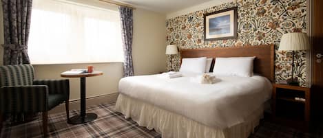 A hotel room with a large bed, a chair, a small table, and a window with curtains.