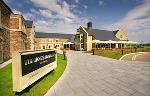 A hotel reception area with a sign for The Hog's Head Inn Alnwick, a brick building with a large patio and outdoor seating.