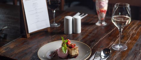 A dessert plate with ice cream and fruit on a wooden table, a menu, salt and pepper shakers, a wine glass, and cutlery.