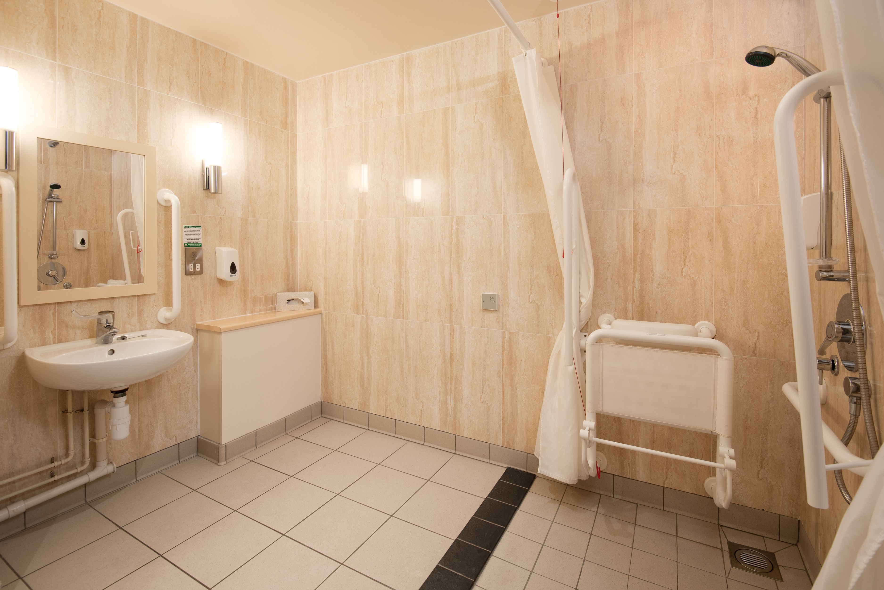 A modern bathroom with a sink, mirror, shower, and grab bars.
