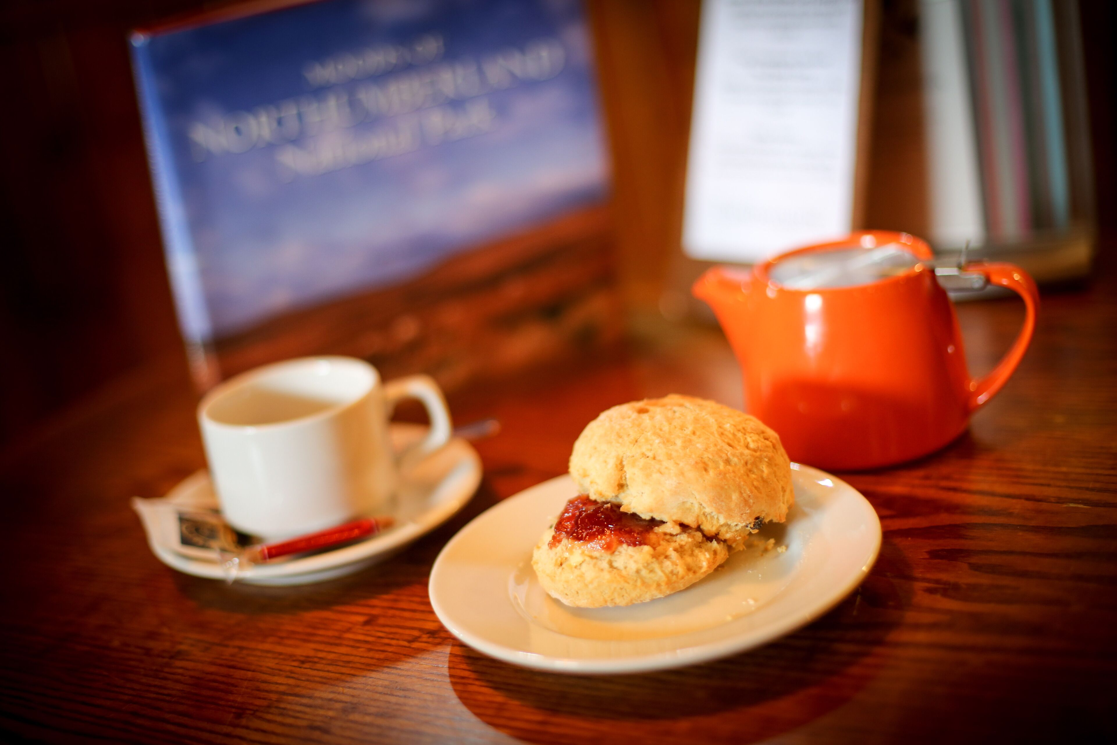 A table with a white cup, a red teapot, and a biscuit on a saucer.
