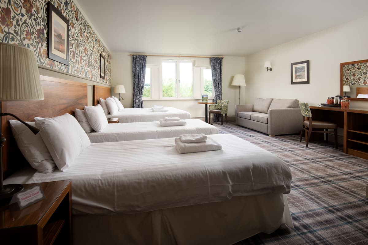 A hotel room with two beds, a sofa, a desk, and a window with curtains.