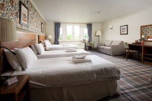 A hotel room with two beds, a sofa, a desk, and a window with curtains.