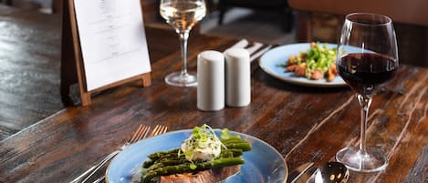 A wooden table with a menu, two glasses of wine, and plates of food.