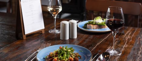 A wooden table with a blue plate of food, two glasses of wine, salt and pepper shakers, and a menu stand.