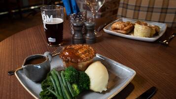Ein Teller mit Kuchen, Kartoffelpüree und grünen Bohnen, ein Bierglas und ein Weinglas auf einem Holztisch.
