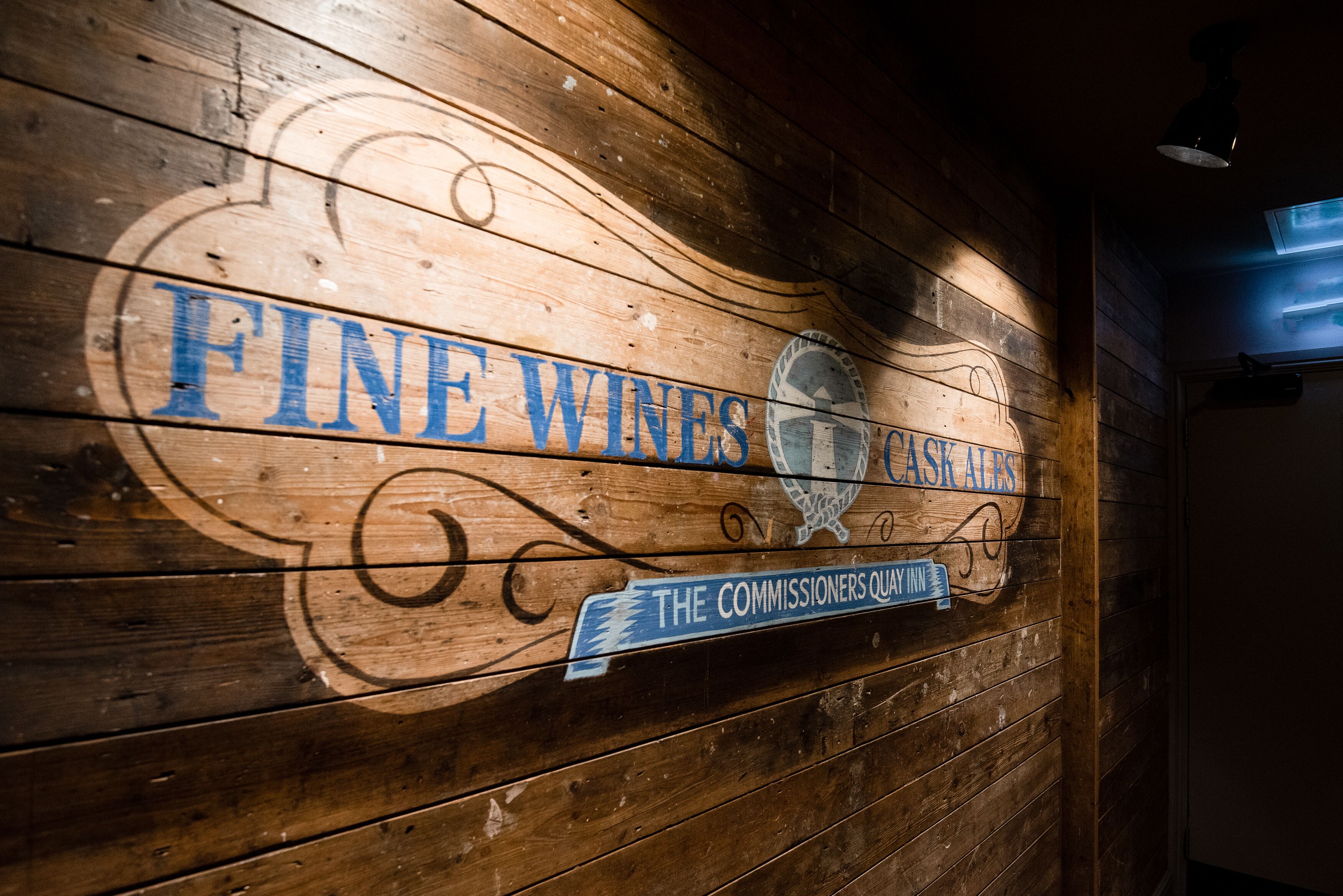 A wooden wall with a sign that reads "FINE WINES & CASKALS" and "THE COMMISSIONERS QUAY INN".