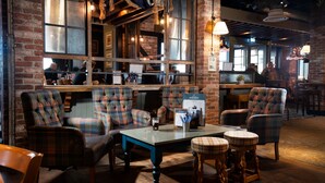 A cozy seating area with plaid upholstered chairs and stools, a wooden table, and a brick wall backdrop. - The Commissioners Quay Inn - The Inn Collection Group (Blyth)