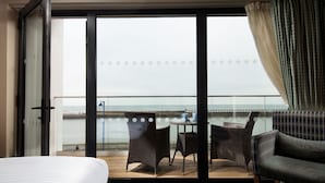A hotel room with a large sliding glass door leading to a balcony with wicker furniture and a view of the sea. - The Commissioners Quay Inn - The Inn Collection Group (Blyth)